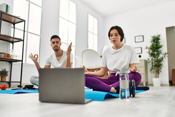 Nuori latinopari tekemässä internet-joogatuntia kannettavan tietokoneen avulla kotona. - Valokuva, kuva