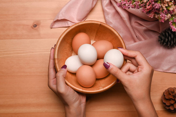 Overhead view young woman arranging eggs into wooden bowl, preparing for Easter celebration. - Foto, afbeelding