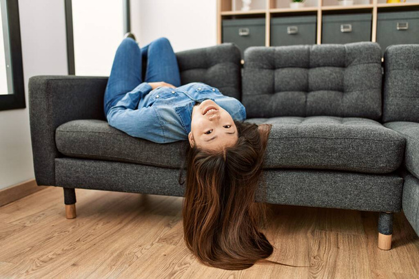 Joven chica china sonriendo feliz acostado en el sofá en casa. - Foto, imagen