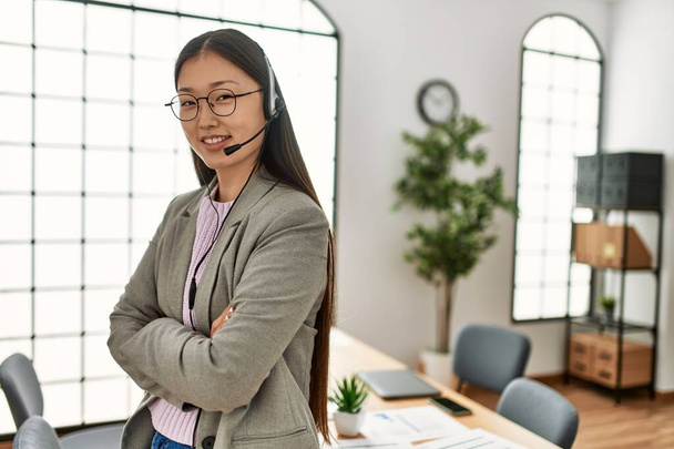 Jeune agent du centre d'appels chinois femme souriante heureuse debout avec les bras croisés geste au bureau. - Photo, image