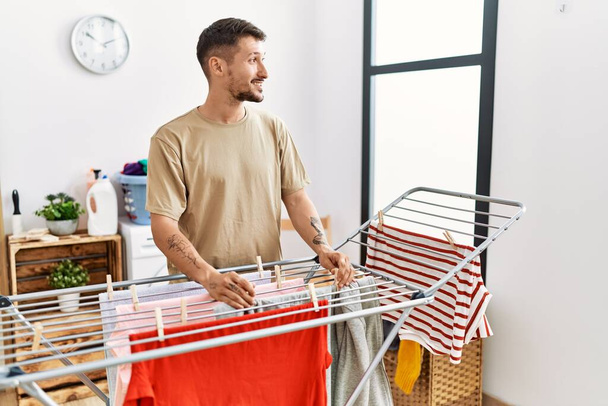 Young hispanic man smilig confident hanging clothes at laundry room - Photo, Image