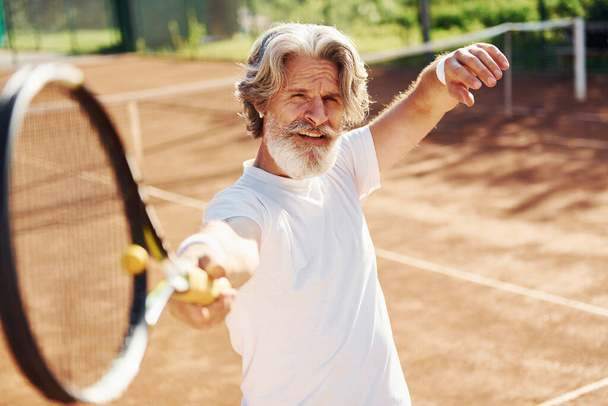 Playing game. Senior modern stylish man with racket outdoors on tennis court at daytime. - Foto, Imagem