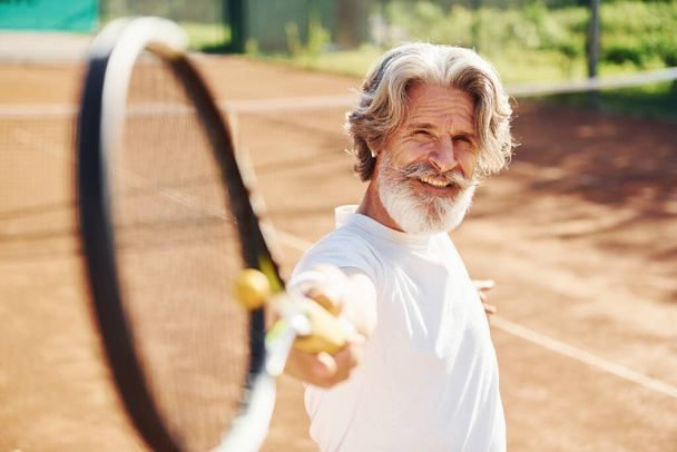 Playing game. Senior modern stylish man with racket outdoors on tennis court at daytime. - Fotó, kép