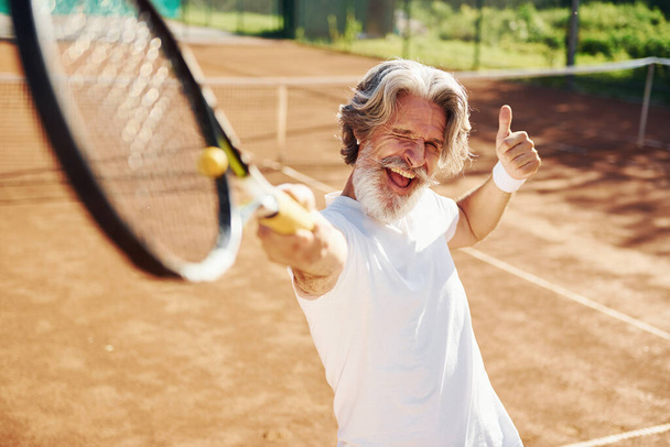 Playing game. Senior modern stylish man with racket outdoors on tennis court at daytime. - Фото, изображение