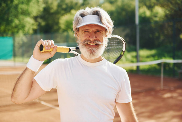 Senior modern stylish man with racket outdoors on tennis court at daytime. - Foto, immagini