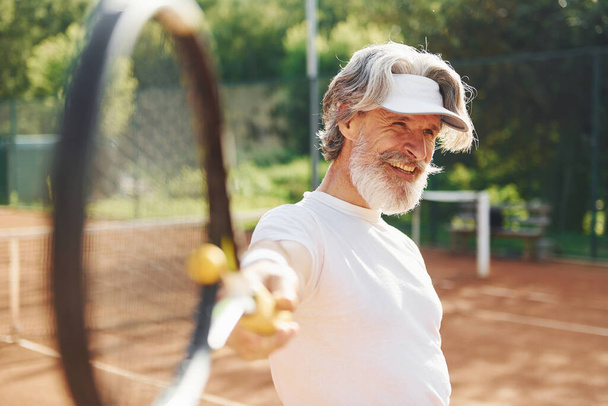 Гра в гру. Старший сучасний стильний чоловік з ракеткою на відкритому повітрі на тенісному корті вдень
. - Фото, зображення