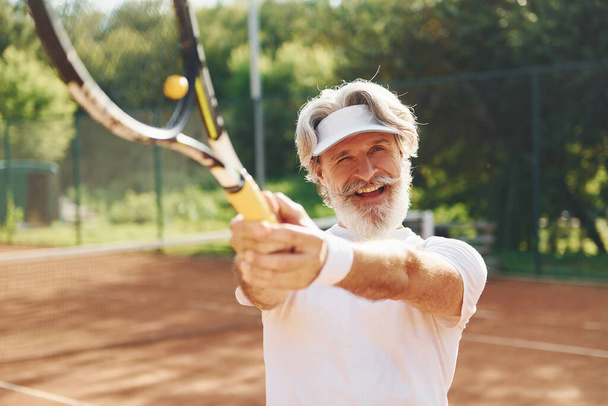 Playing game. Senior modern stylish man with racket outdoors on tennis court at daytime. - Photo, image