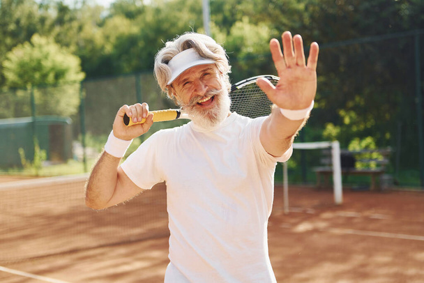 Senior modern stylish man with racket outdoors on tennis court at daytime. - Foto, immagini
