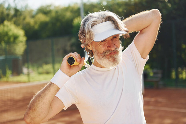 Senior modern stylish man with racket outdoors on tennis court at daytime. - Foto, imagen
