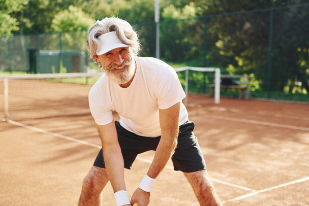 Playing game. Senior modern stylish man with racket outdoors on tennis court at daytime. - Foto, afbeelding