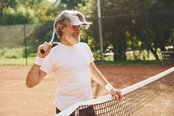 Senior modern stylish man with racket outdoors on tennis court at daytime. - Photo, image
