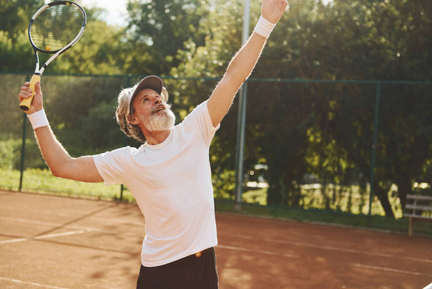 Playing game. Senior modern stylish man with racket outdoors on tennis court at daytime. - Foto, immagini