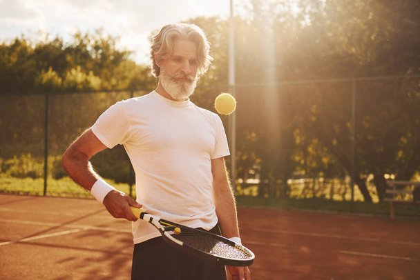 Training time. Senior modern stylish man with racket outdoors on tennis court at daytime. - 写真・画像