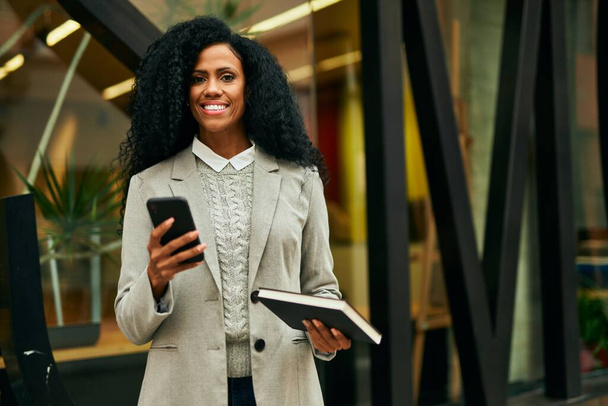 Mulher de negócios afro-americana de meia-idade usando o livro de retenção de smartphones na cidade. - Foto, Imagem