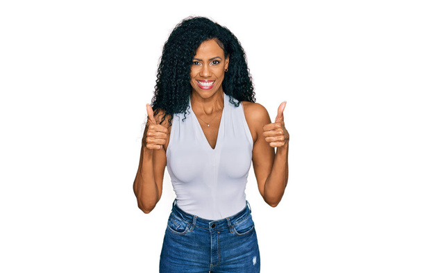 Middle age african american woman wearing casual style with sleeveless shirt success sign doing positive gesture with hand, thumbs up smiling and happy. cheerful expression and winner gesture.  - Fotó, kép