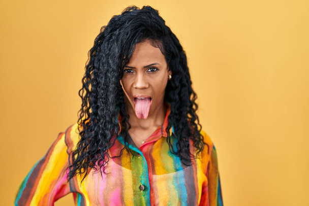 Middle age hispanic woman standing over yellow background sticking tongue out happy with funny expression. emotion concept.  - Photo, Image