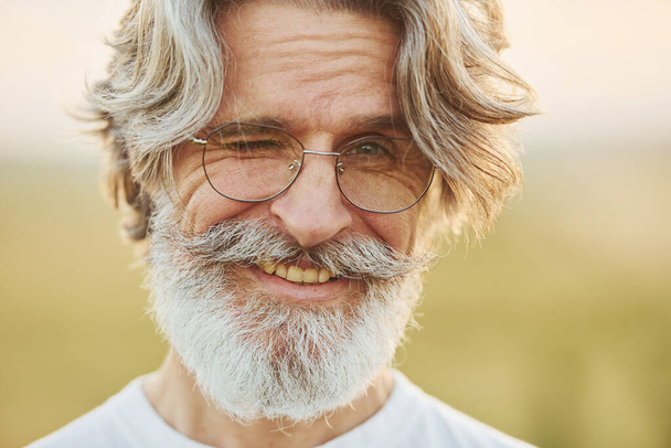 Portrait of seenior stylish man with grey hair and beard that standing outdoors on field at sunny day. - Φωτογραφία, εικόνα