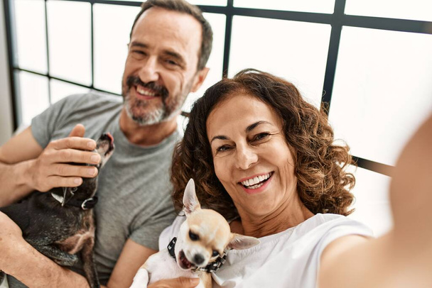 Middelbare leeftijd Latijns-Amerikaans koppel glimlachend gelukkig selfie maken door de camera. Liggend op het bed met honden thuis. - Foto, afbeelding