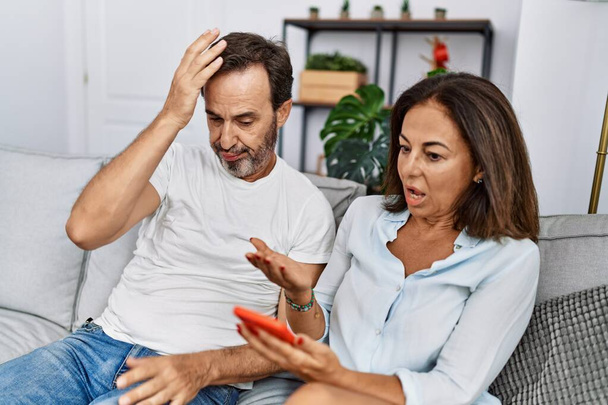 Hombre y mujer de mediana edad pareja con problemas de infidelidad utilizando el teléfono inteligente en casa - Foto, imagen