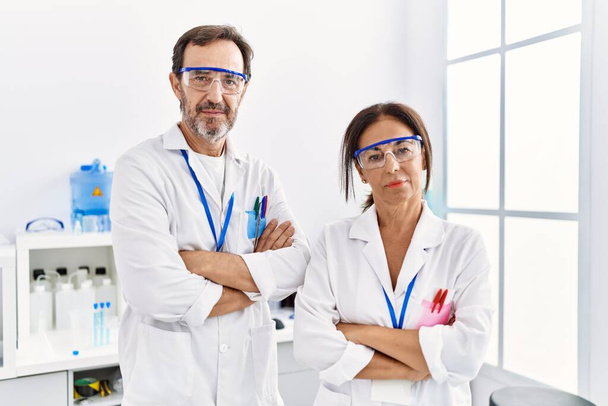 Homem e mulher parceiros de meia-idade vestindo uniforme cientista de pé com braços cruzados gesto no laboratório - Foto, Imagem