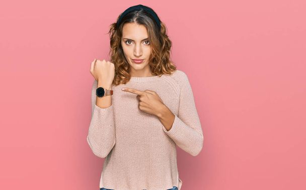 Beautiful young caucasian woman wearing casual sweater in hurry pointing to watch time, impatience, looking at the camera with relaxed expression  - Photo, image