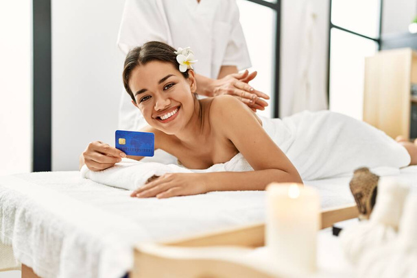 Young latin woman relaxed having back massage holding credit card at beauty center - Zdjęcie, obraz