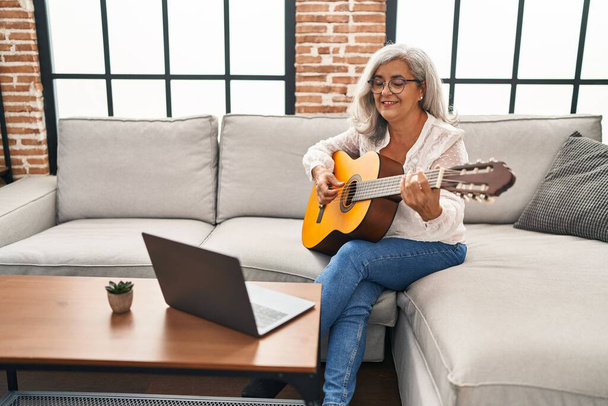 Orta yaşlı bir kadının evde online gitar dersi var. - Fotoğraf, Görsel