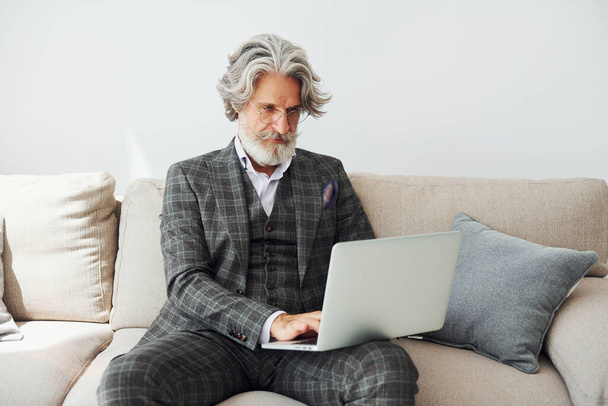 In apartment with elegant clothes. Senior stylish modern man with grey hair and beard indoors. - Фото, зображення