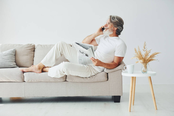 Sits on the sofa. Senior stylish modern man with grey hair and beard indoors. - Photo, Image