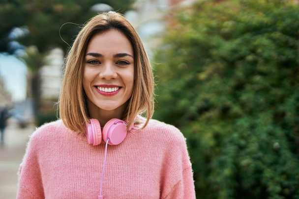 Jeune fille caucasienne souriant heureux en utilisant des écouteurs à la ville. - Photo, image