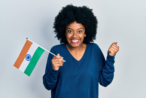 Jeune femme afro-américaine tenant le drapeau de l'Inde criant fier, célébrant la victoire et le succès très excité avec le bras levé  - Photo, image