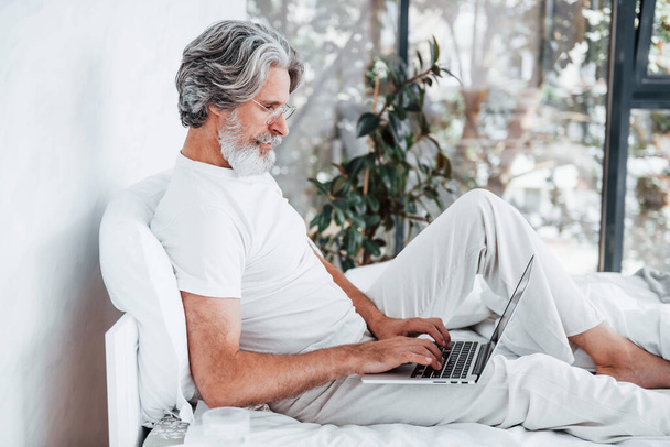 Laptop on legs. Senior stylish modern man with grey hair and beard indoors. - Fotografie, Obrázek