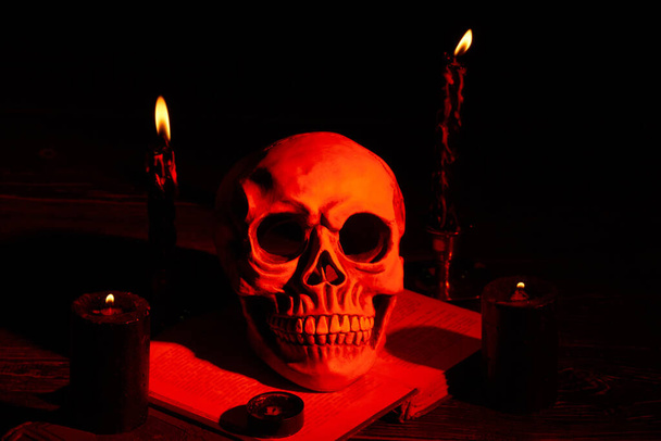Crâne humain et bougies avec lumière orange dans l'obscurité. - Photo, image