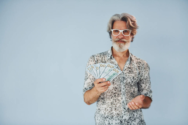 Мільйонер з готівкою в руках. Старший стильний сучасний чоловік з сірим волоссям і бородою в приміщенні
. - Фото, зображення