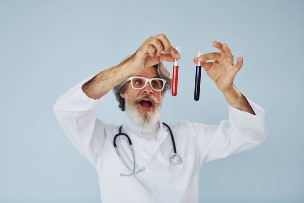 Doctor holds test tubes. Senior stylish modern man with grey hair and beard indoors. - Фото, зображення