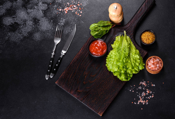 A wooden cutting board with a kitchen knife with spices and herbs on a dark concrete background. Cooking at home - Foto, afbeelding