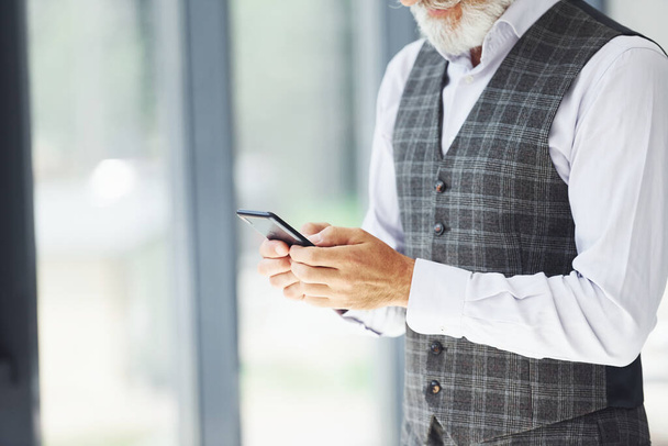 Successful businessman uses phone. Senior stylish modern man with grey hair and beard indoors. - Φωτογραφία, εικόνα