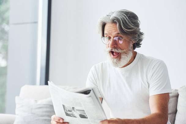 Having a rest on the sofa. Senior stylish modern man with grey hair and beard indoors. - Foto, Imagen