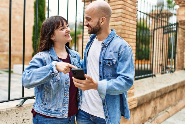 若いヒスパニック系のカップルは、市内でスマートフォンを使用して幸せな笑顔. - 写真・画像