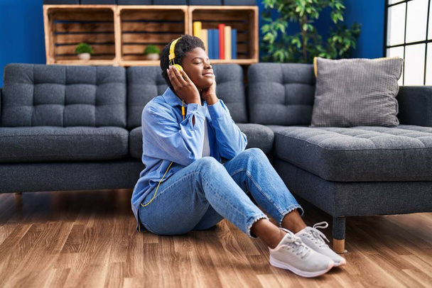 African american woman listening to music sitting on floor at home - Fotó, kép