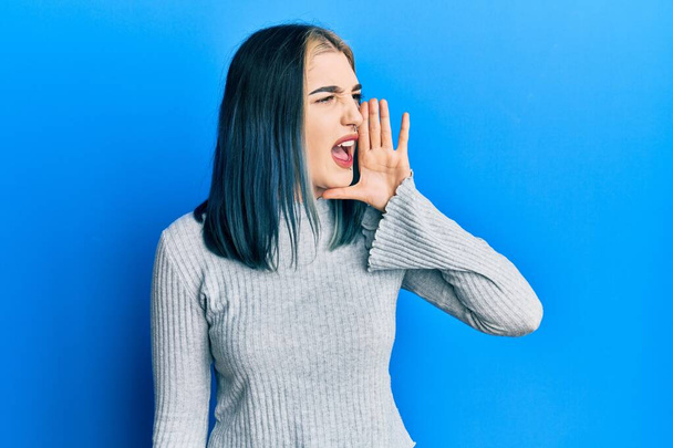 若い現代の少女はカジュアルなセーターを着て大声で叫び、口の中で手で横に大声で叫ぶ。コミュニケーションの概念.  - 写真・画像