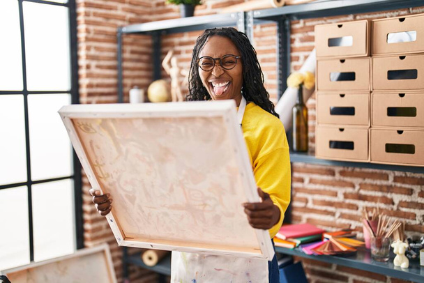 Mujer africana mirando el lienzo del pintor sacando la lengua feliz con expresión divertida.  - Foto, imagen