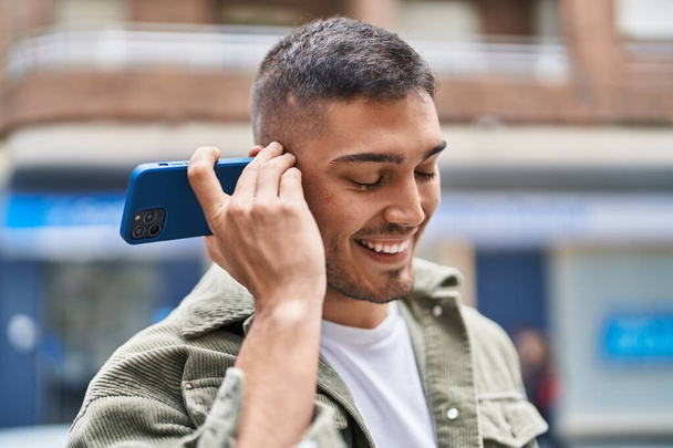 Giovane uomo ispanico sorridente fiducioso messaggio audio di ascolto dallo smartphone in strada - Foto, immagini