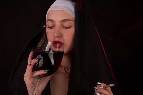 Κακό κορίτσι που φοράει καθολική κουκούλα και πίνει κόκκινο κρασί . - Φωτογραφία, εικόνα