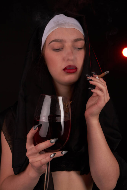 いたずらなセクシー修道女の女の子喫煙タバコとドリンクワインの肖像. - 写真・画像