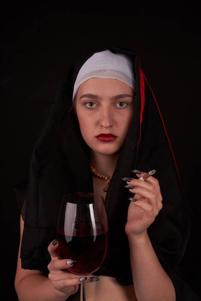 Portret van een jonge stoute non met een glas wijn en een sigaret. - Foto, afbeelding