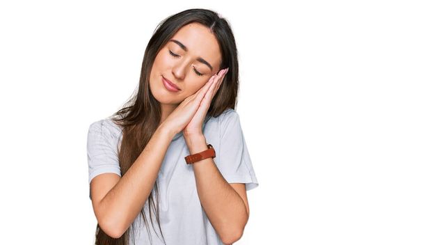 Young hispanic girl wearing casual white t shirt sleeping tired dreaming and posing with hands together while smiling with closed eyes.  - Photo, Image