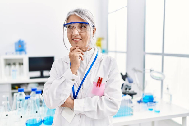 Mujer de pelo gris de mediana edad vistiendo uniforme científico de pie con los brazos cruzados gesto en el laboratorio - Foto, imagen