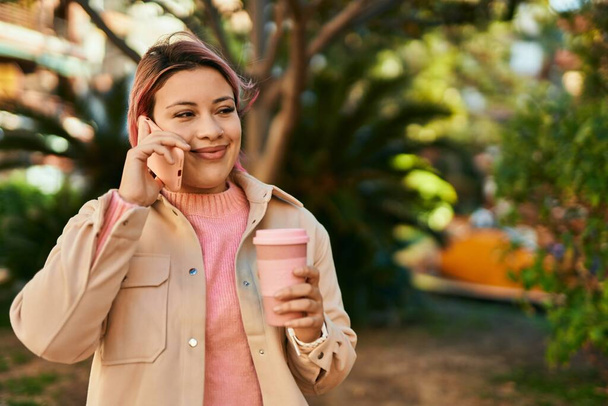 Young hispanic girl talking on the smartphone and drinking coffee at the city. - Foto, Imagen