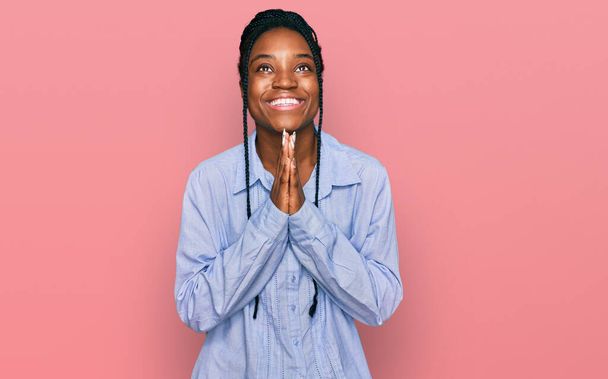 Jonge Afro-Amerikaanse vrouw draagt casual kleding bedelen en bidden met de handen samen met hoop uitdrukking op het gezicht zeer emotioneel en bezorgd. bedelen.  - Foto, afbeelding
